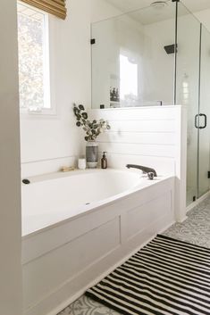 a white bath tub sitting under a window next to a rug on the floor in a bathroom