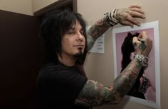 a man with black hair and tattoos holding his arm up in front of a mirror