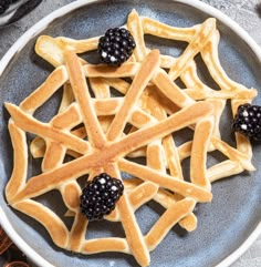 a plate with waffles and blackberries on it next to some cinnamon sticks