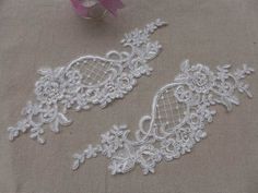 two pieces of white lace with flowers and hearts on them, sitting next to a pink ribbon