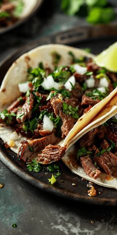 two tacos with meat, onions and cilantro on a plate next to a lime