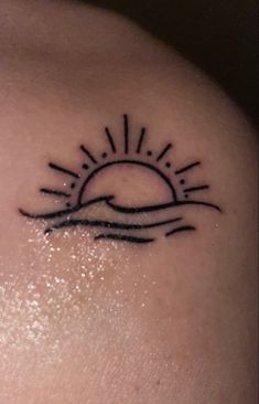 a small sun tattoo on the back of a woman's shoulder, with waves