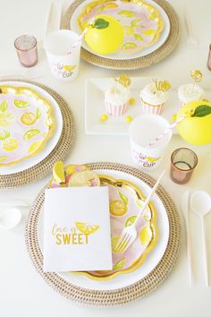 the table is set with yellow and pink plates, napkins, silverware, and cupcakes