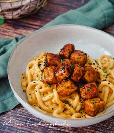 a white bowl filled with noodles and meatballs on top of a wooden table next to a green napkin