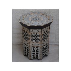 an ornately decorated side table in front of a white brick wall with black trim