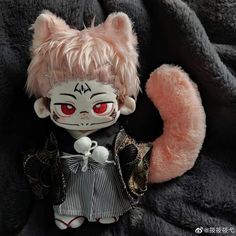 a stuffed animal doll with red eyes and pink hair sitting on a black blanket next to a teddy bear