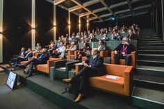 a group of people sitting on orange couches in an auditorium