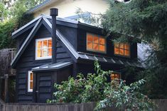 a small black house with orange windows in the front yard and trees around it,