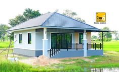 a small house with a blue roof and black railings on the front porch is surrounded by green grass