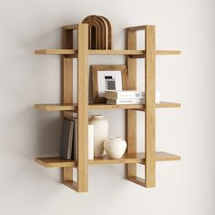 a wooden shelf with books, vases and other items on it against a white wall