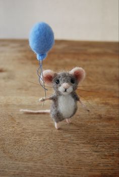 a tiny mouse holding a blue balloon on top of a wooden table