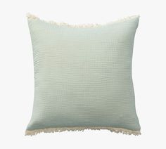 a light green pillow with fringes on the edges and an off white back ground