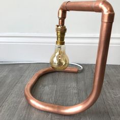 a copper colored lamp with a light bulb on it's side, sitting on the floor