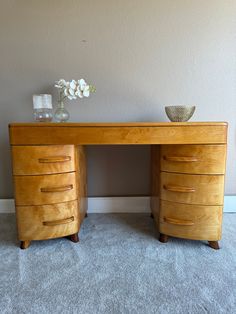 a wooden desk with two vases on top of it next to a gray wall