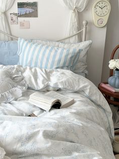 an open book is laying on the bed with white sheets and blue striped pillows,