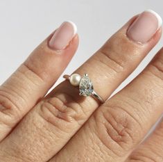 a close up of a person's hand with a diamond and pearl ring on it