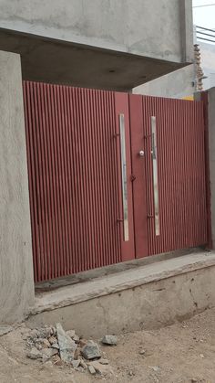 an open red door on the side of a concrete building next to a pile of rubble