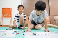 two young boys sitting on the floor playing with paper and crayons in front of them