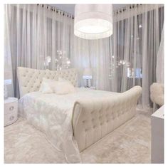 a white bed sitting in a bedroom next to a window covered in sheer drapes