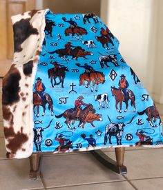 a cow print blanket on top of a chair with horses and cows on blue fabric