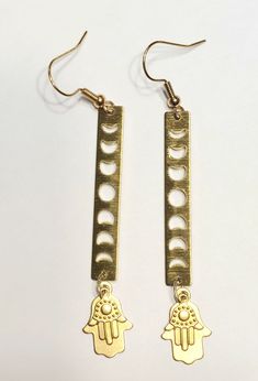 pair of brass earrings with hamsa and moon design on them, hanging from hooks