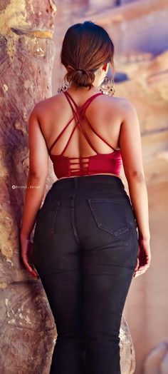 a woman standing next to a stone wall with her back turned towards the camera and wearing black jeans