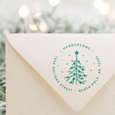 a white envelope with a green christmas tree stamp on the front and bottom, sitting next to evergreen branches