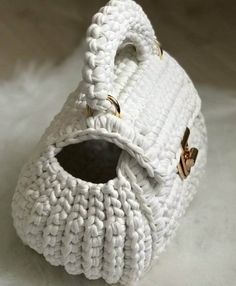 a crocheted white basket with gold handles on a white surface in the shape of a baby's boot