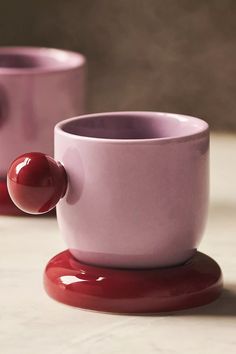 two pink cups with red handles and one has a cherry on the side, sitting next to each other