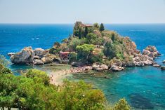 an island in the middle of the ocean surrounded by trees and people walking on it