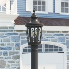 a lamp post in front of a house with a garage door and stone wall behind it