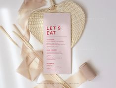 a pink menu card sitting on top of a white table next to some straws