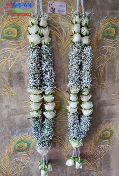 two vases with white flowers hanging from strings on a peacock wallpapered background