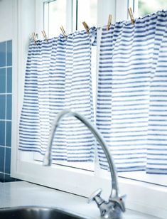 a kitchen sink under a window with blue and white striped curtains hanging on the windowsill