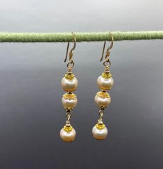 Unique presentation of peach freshwater pearls, antique gold spacers, and filigree bead caps in these elegant dangle earrings. The dangles are connected to each other and to the gold filled earwire through gold filled wrapped loops.  The earrings are about 1 1/4 inches long, measured from the earwire, and come nestled comfortably on a bed of cotton in a white cardboard box. Made in the USA by me. NA-821-0624-1111 Pearl Earrings With Gold Beads For Gift, Elegant Rose Gold Earrings With Dangling Beads, Gold Beaded Pearl Earrings, Gold Pearl Earrings With Gold Beads, Gold Pearl Charm Earrings, Pearl Drop Earrings With Gold Beads, Elegant Gold Beaded Pearl Earrings, Elegant Gold Beaded Chandelier Earrings As Gift, Delicate Gold Earrings With Dangling Beads