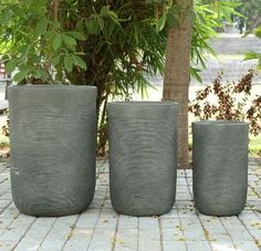 three cement planters sitting on top of a brick floor next to a tree and bushes