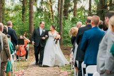 a bride and groom walking down the aisle at their outdoor wedding ceremony in the woods