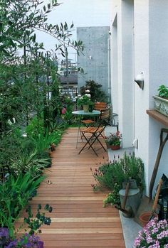 a wooden deck surrounded by potted plants and flowers on the side of a building