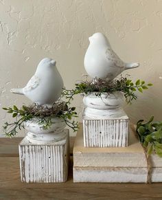 two white ceramic birds sitting on top of books with greenery in their beaks