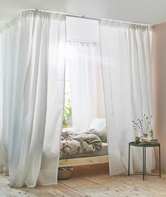 a bed sitting under a window next to a white curtain in a room with wooden floors