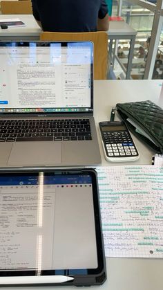 two laptops sitting on top of a table next to papers and calculators