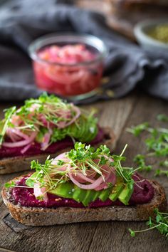 two slices of bread topped with veggies and sprouts on a wooden table