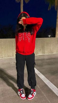 a woman in red hoodie and black pants standing next to palm trees at night