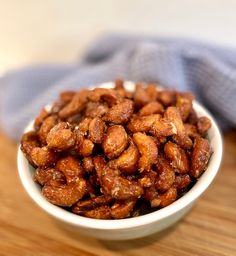 a white bowl filled with nuts sitting on top of a wooden table next to a blue towel