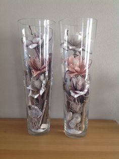 two clear vases with flowers in them sitting on a wooden table next to a wall