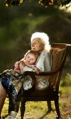 an old woman sitting on a chair holding a small child in her lap and looking at the camera