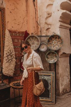 a woman standing in front of a store with plates and bowls on the wall behind her