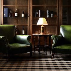 two green leather chairs sitting next to each other in front of a wooden bookcase