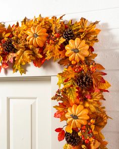 a wreath made out of fake leaves and pumpkins hanging on the front door for fall