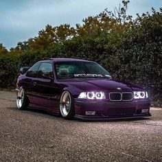 a purple car parked on the side of a road next to some bushes and trees